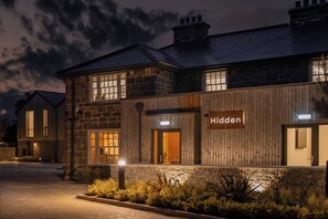 A stone building with a wooden facade, a sign reading 'Hidden,' and a well-lit entrance. - Hidden 19- Coastal Hot Tub (St Ives)
