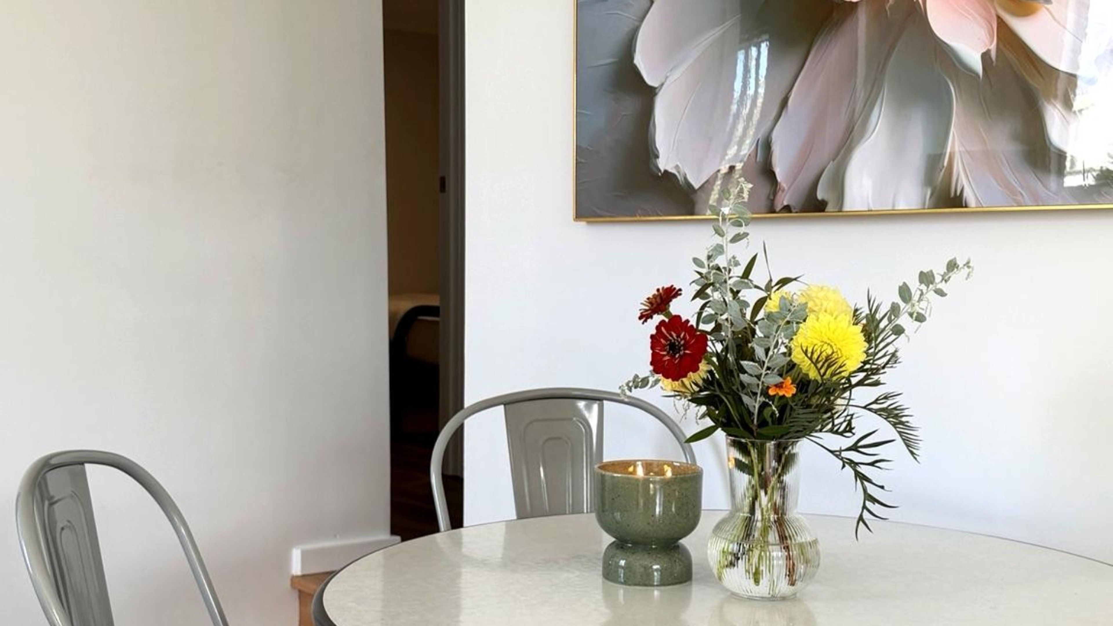 Una mesa de comedor con un florero, una vela y una silla.