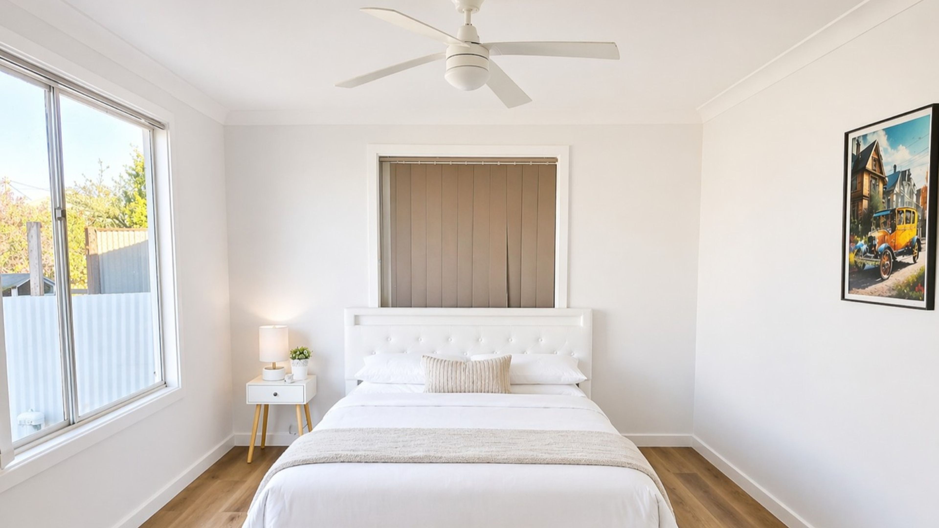 Ein Schlafzimmer mit einem Bett, einem Nachttisch, einem Deckenventilator, einem Fenster und einem Bild an der Wand.