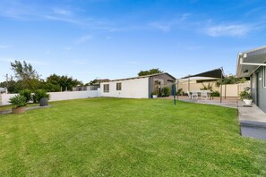 Un patio trasero residencial con un césped cuidado, un área de patio con mobiliario exterior y un cobertizo pequeño.