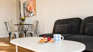 A dining area with a white table, clear chairs, a plate of pastries, and a blue checkered mug.