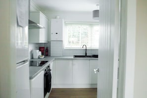 A compact kitchen with white cabinets, a built-in oven, a dishwasher, and a window with blinds. - Renfrew Town Centre, sleeps 6 - Pass the Keys (Renfrew)