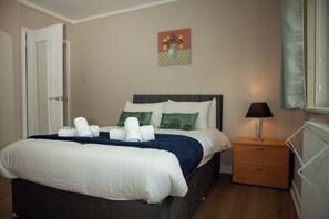 A neatly made bed with pillows and a blanket, a bedside table with a lamp, and a wall painting. - Renfrew Town Centre, sleeps 6 - Pass the Keys (Renfrew)