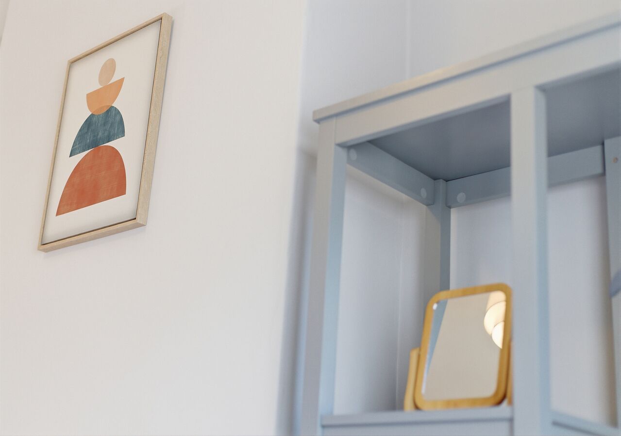 Ein gerahmtes abstraktes Kunstwerk an der Wand, ein Spiegel auf einem blauen Regal und eine weiße Wand.