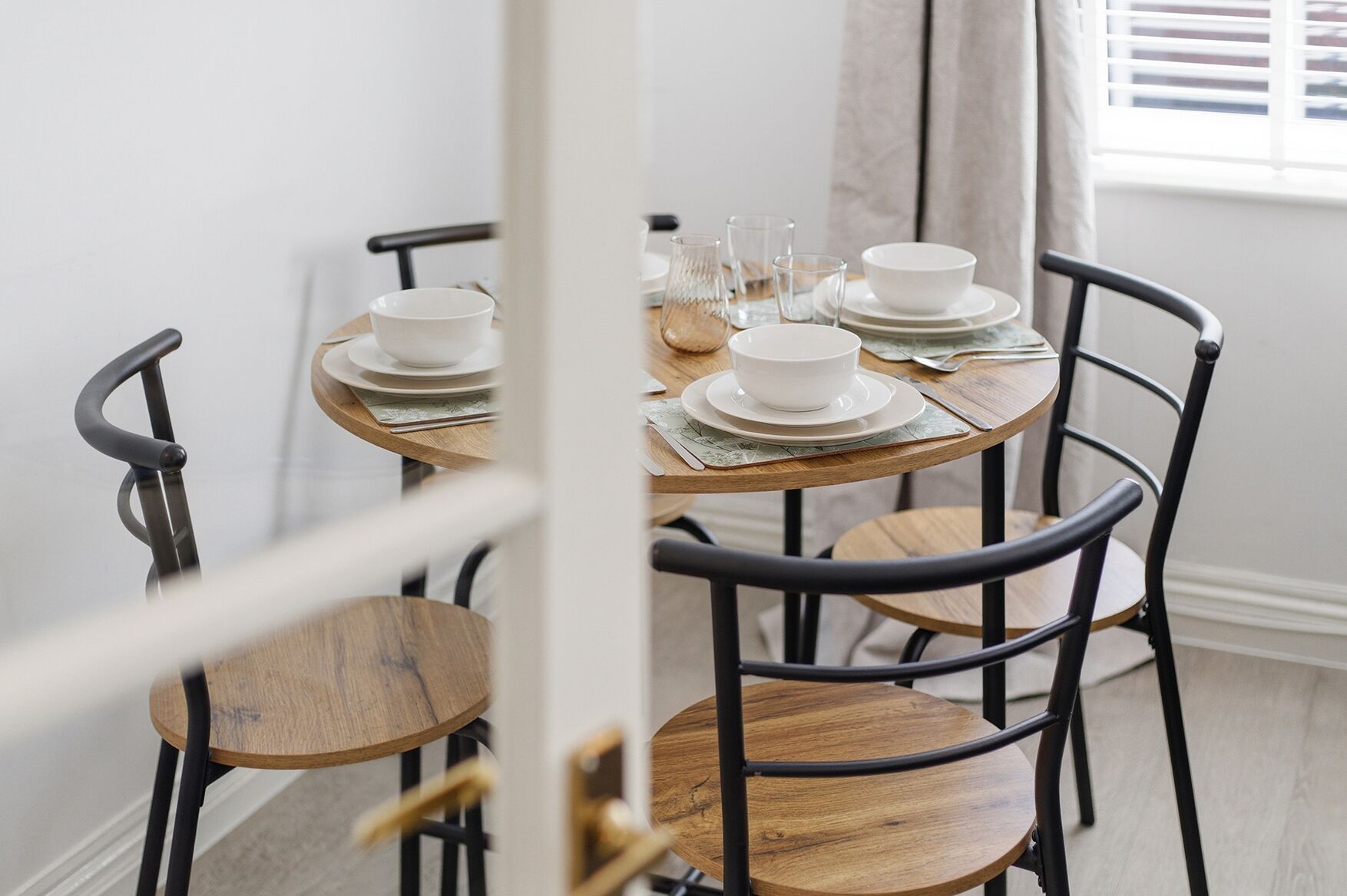 A dining area with round tables and chairs, white plates, and clear glasses.