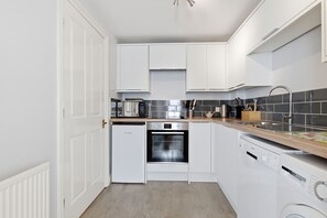 Una cocina compacta con armarios blancos, horno empotrado, lavavajillas y una encimera con tostadora y cafetera.