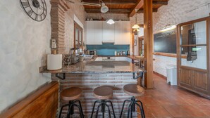Une cuisine avec un îlot central en briques, des tabourets de bar, une horloge et un tableau noir servant de menu.