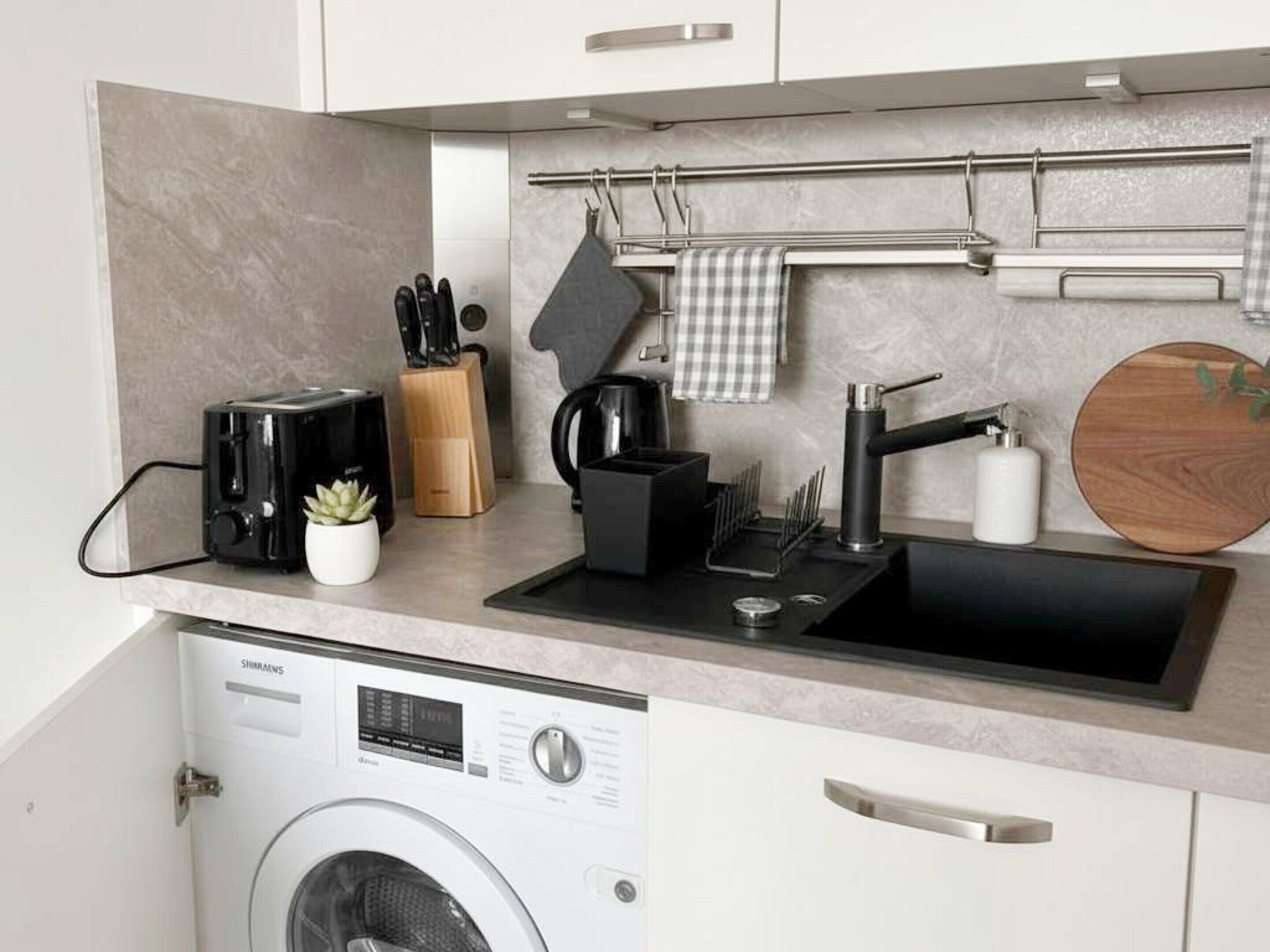 A compact kitchen with a washing machine, a toaster, a coffee maker, and a knife block.