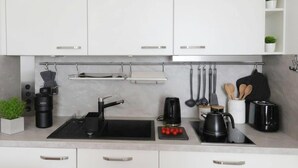 A modern kitchen with white cabinets, a black countertop, a kettle, a coffee maker, and a cutting board with tomatoes. - Sunny Stay in Alexanderplatz (Berlin)