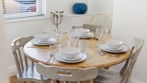 Ein runder Holztisch mit weißen Tellern, klarem Glas und Besteck.