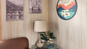 A room with wooden walls, a brown leather couch, a glass table with a lamp, and a wall-mounted sign.