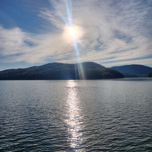 A calm lake with sunlight reflecting on the water, surrounded by hills.