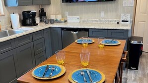 A kitchen with a wooden table set for four, a coffee maker, and a TV mounted above the counter.