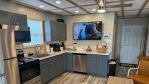 A modern kitchen with stainless steel appliances, grey cabinets, and a large TV mounted above the counter.