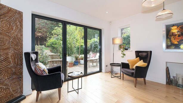 A spacious room with large windows, a black chair, a round table, and a lamp. - Stunning South London Home with Rare Garden Oasis - Pass the Keys (London)