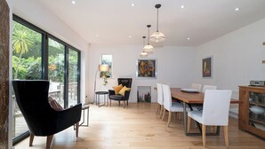 A spacious dining area with a wooden table and chairs, a black armchair, and pendant lighting. - Stunning South London Home with Rare Garden Oasis - Pass the Keys (London)