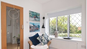 A room with a wicker chair, a radiator, a window with a view of greenery, and wall art. - Stunning South London Home with Rare Garden Oasis - Pass the Keys (London)