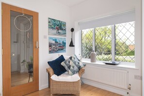A room with a wicker chair, a radiator, a window with a view of greenery, and wall art. - Stunning South London Home with Rare Garden Oasis - Pass the Keys (London)