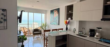 A modern kitchen with a dining area, large windows, and a view of the sea.