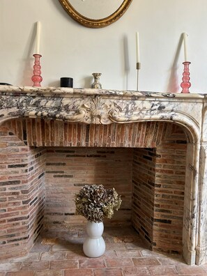 Une cheminée avec un manteau en marbre, un vase rempli de fleurs séchées et des bougies.