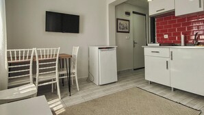 A compact kitchen with white cabinets, a small refrigerator, and a dining area with white chairs. - İzan Villa Bakış Apart Otel (Bodrum)
