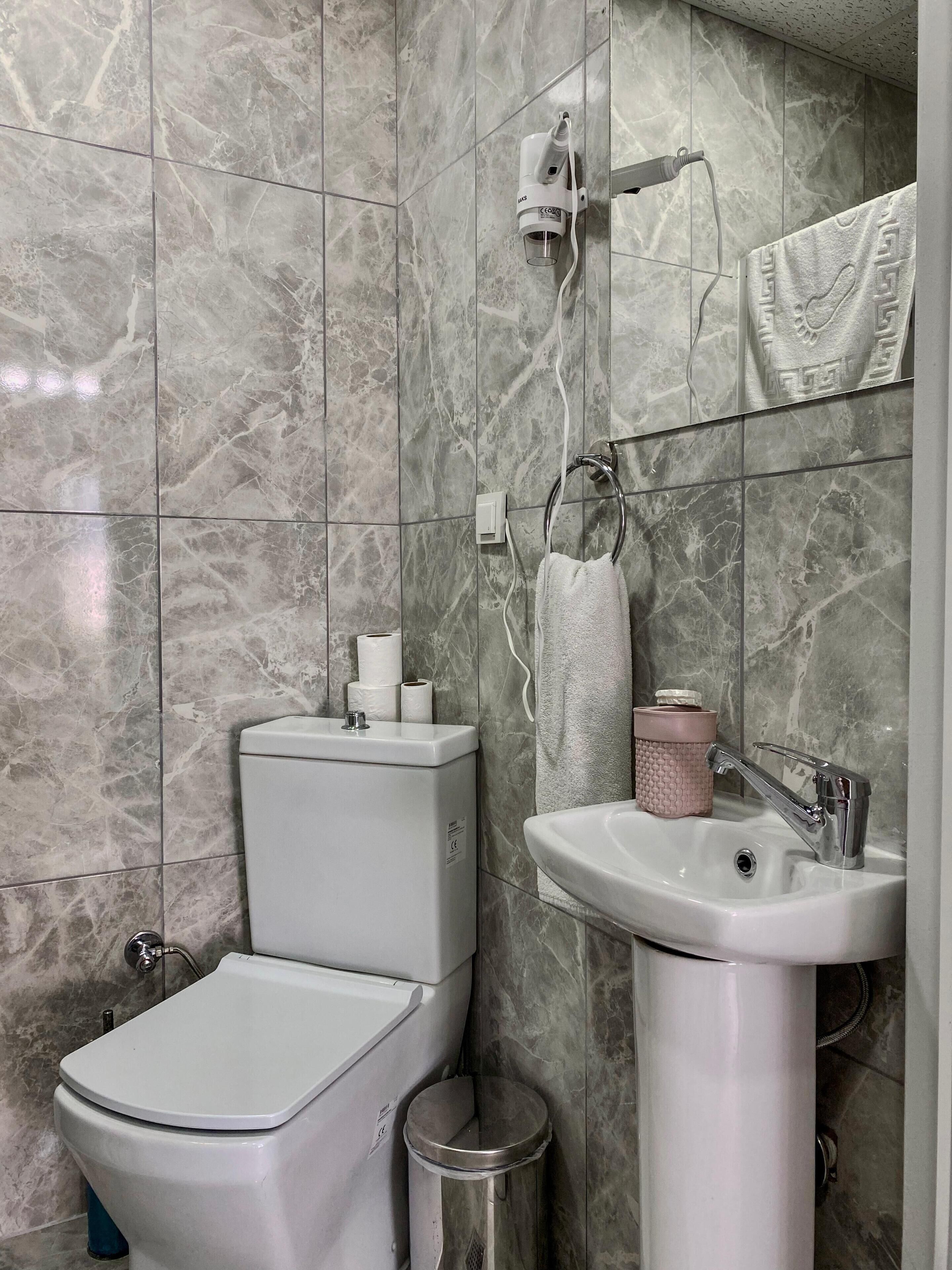 A bathroom with a toilet, sink, towel rack, and a hairdryer mounted on the wall.