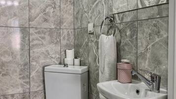 A bathroom with a toilet, sink, towel rack, and a hairdryer mounted on the wall.