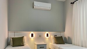 A hotel room with two beds, a bedside table, an air conditioning unit, and wall-mounted lighting. - İzan Villa Bakış Apart Otel (Bodrum)