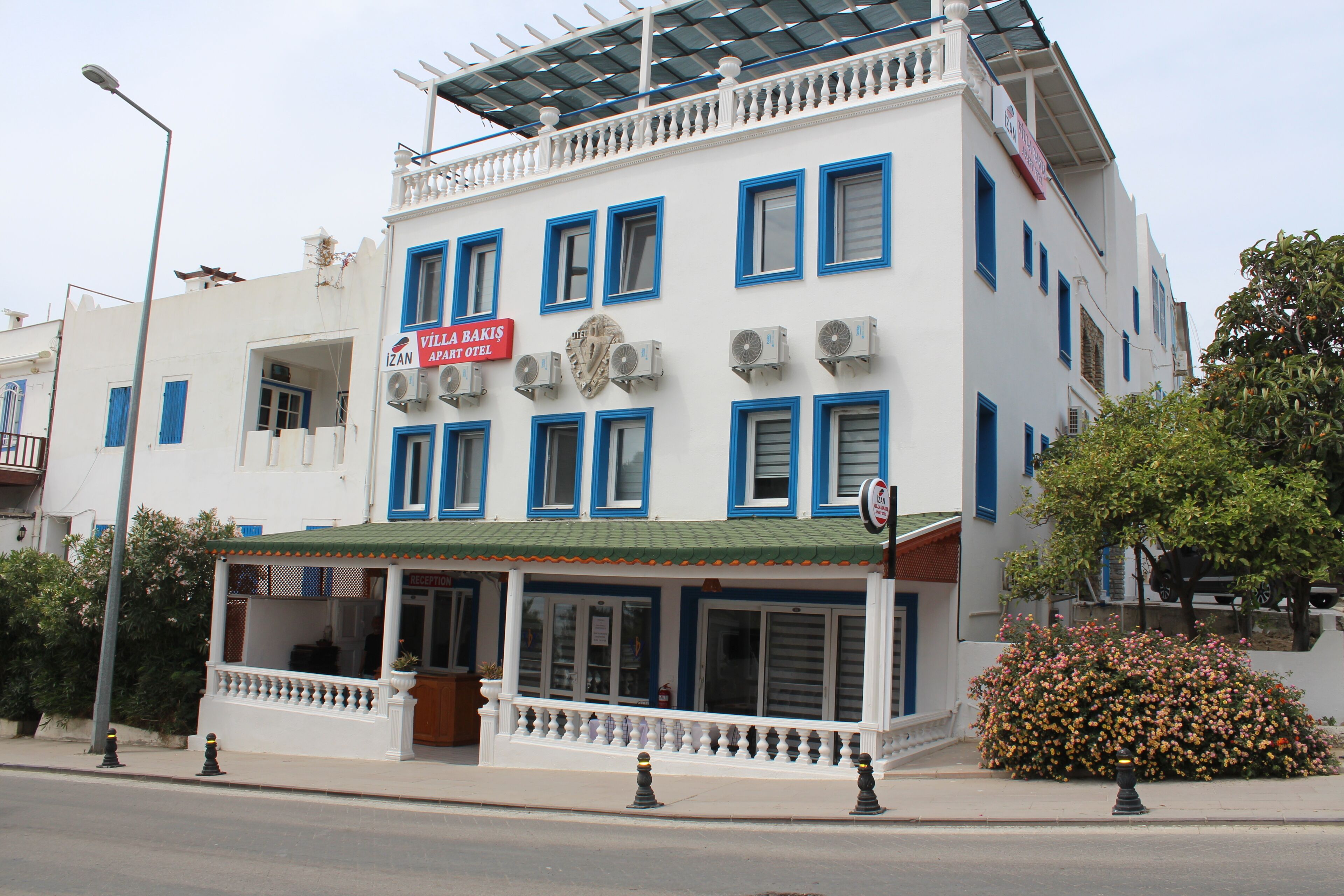 A white building with blue accents, multiple air conditioning units, and a sign for 'Villa Bakis Apart Hotel.'