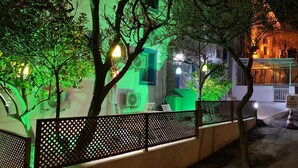 A nighttime view of a building with a green-lit exterior, a fence, and a sign for 'IZAN VILLA BAKIS.' - İzan Villa Bakış Apart Otel (Bodrum)