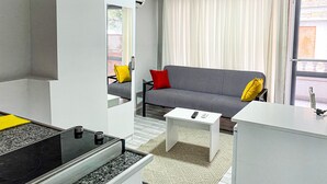A modern living room with a sofa, a coffee table, and a kitchen area with a stove. - İzan Villa Bakış Apart Otel (Bodrum)