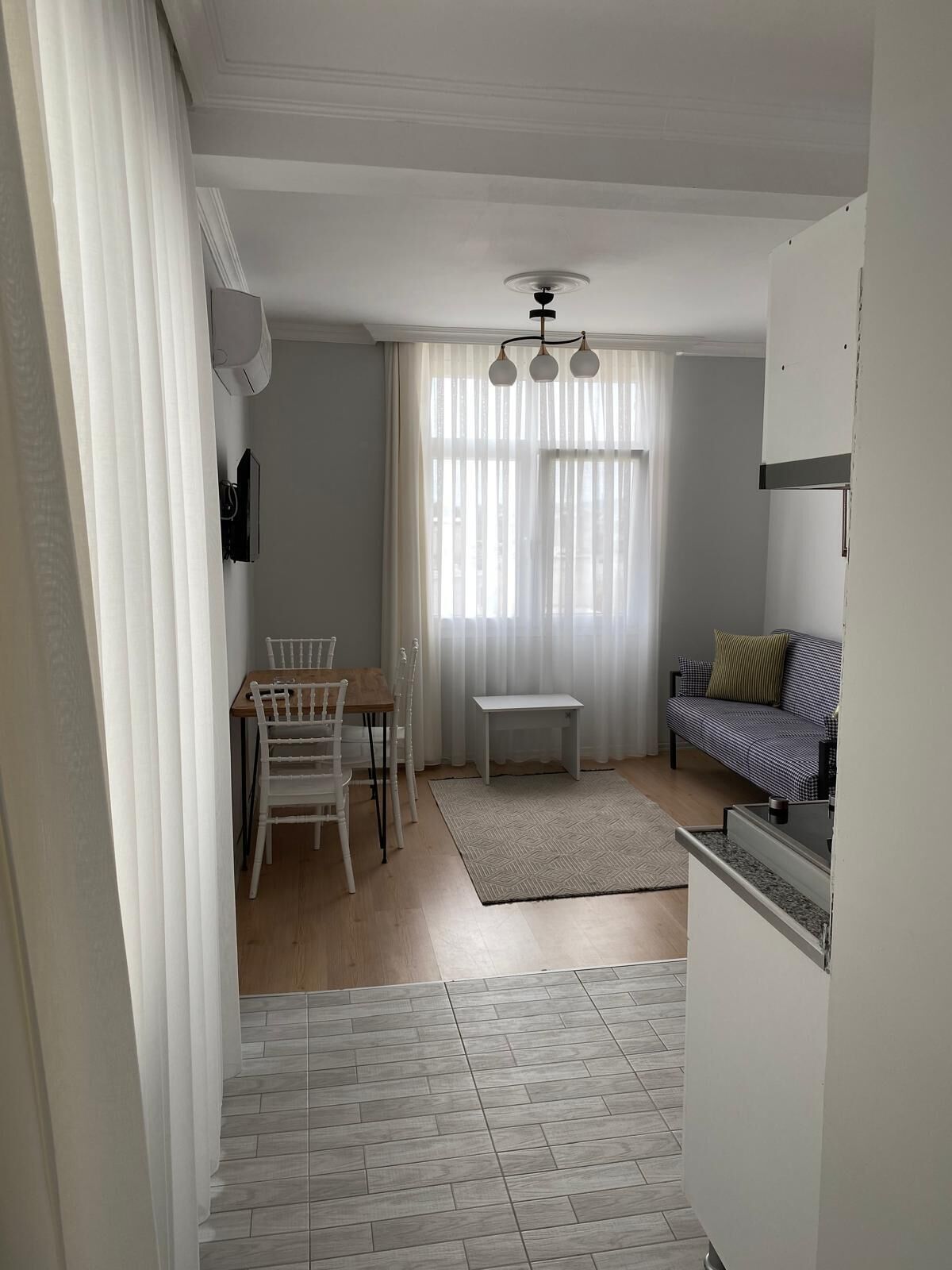 Un salon comprenant une table à manger, des chaises, un canapé, une petite table blanche et un ventilateur de plafond.