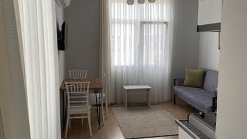 Un salon comprenant une table à manger, des chaises, un canapé, une petite table blanche et un ventilateur de plafond.