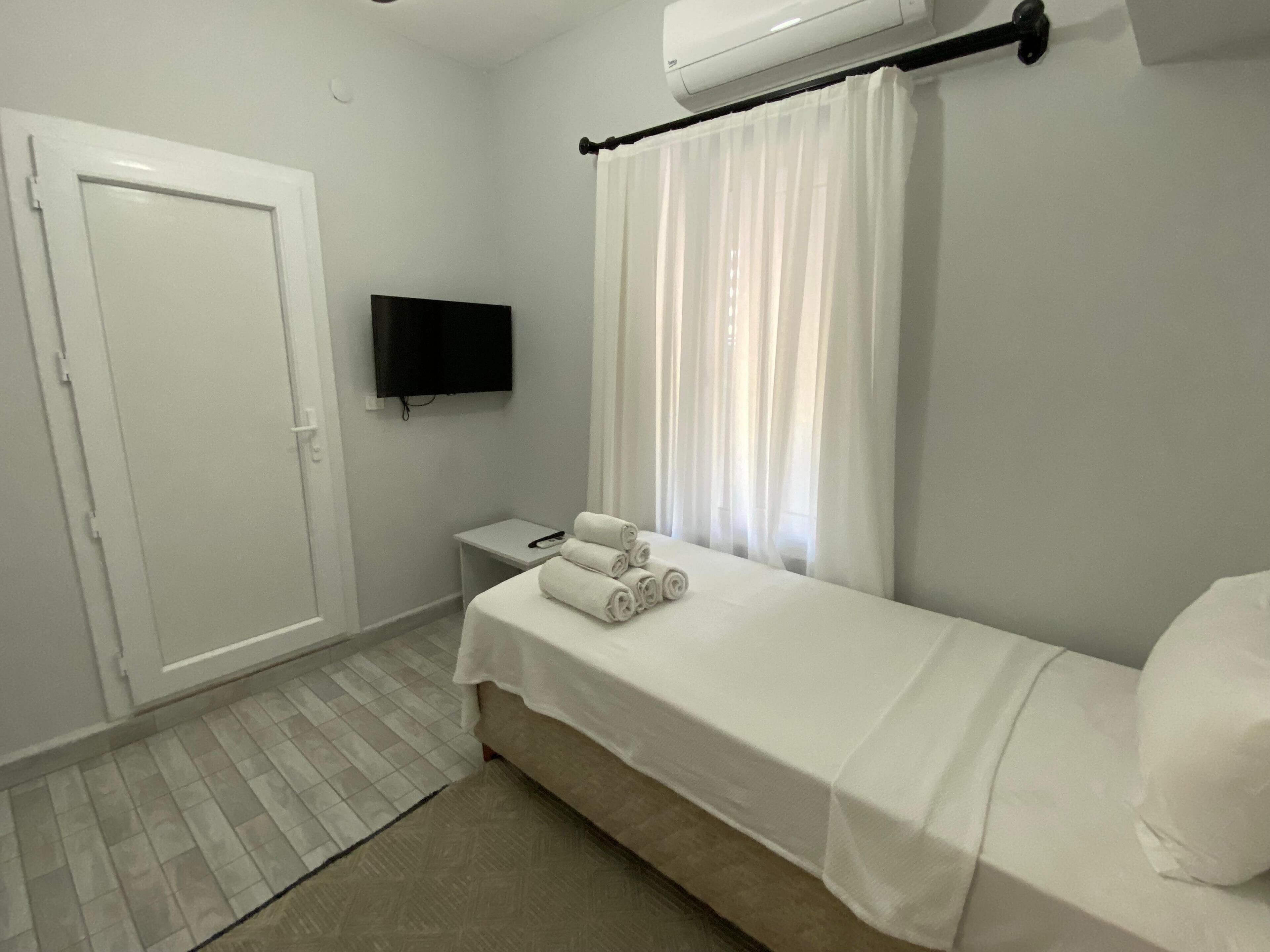 Een slaapkamer met een bed, een televisie, een raam met gordijnen, een deur en een airconditioningsunit.