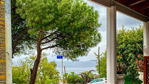 A balcony with a view of the sea, a tree, and parked cars. - İzan Villa Bakış Apart Otel (Bodrum)