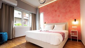 A hotel room with a large bed, a suitcase, a window with curtains, and a wall-mounted light. - Acropolis Promenade by Teknys Hosting (Athina)
