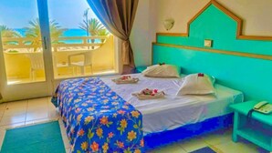 A hotel room with a bed, a bedside table, a view of the sea, and a balcony with chairs.