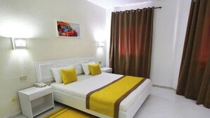 A hotel room with a bed, nightstands, a bedside table, a window with curtains, and a wall-mounted light.