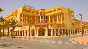 A multi-story hotel with a yellow facade, multiple balconies, and a central entrance with a sign.