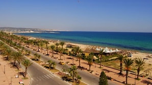 A coastal road with palm trees, a beach, and a clear blue sky.