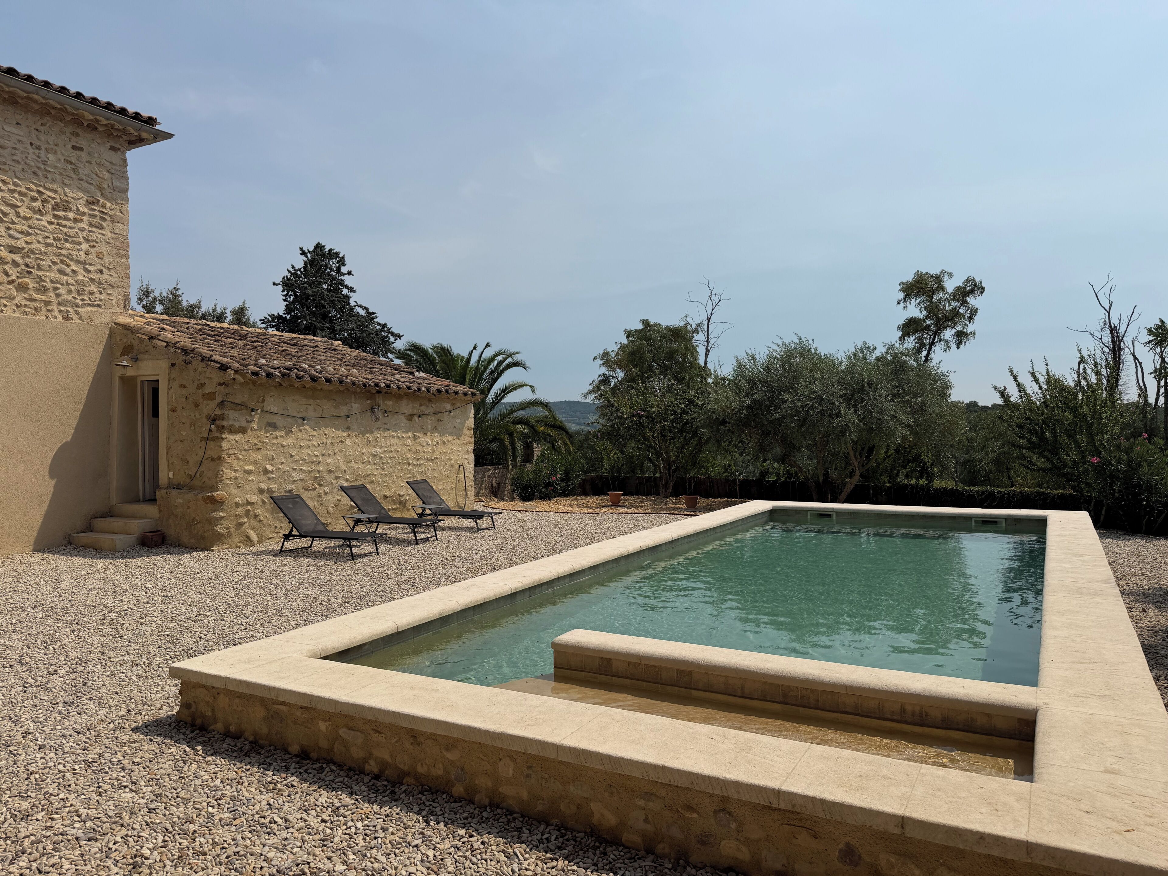 A swimming pool with a stone deck, a small stone building, and lounge chairs.