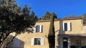 Un edificio in pietra con vialetto sterrato, un albero alto e posti a sedere all'aperto.
