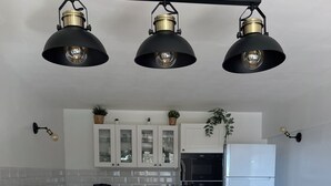 Una cucina con schienale in pietra, mobili bianchi, frigorifero nero e tre lampade a sospensione.