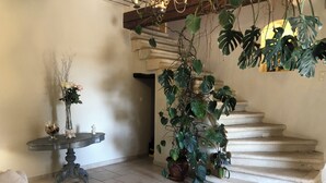 Un soggiorno con divano, un tavolo con un vaso di fiori, una scala e piante in vaso.