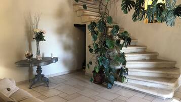 Un salon avec un canapé, une table ornée d’un vase de fleurs, un escalier et des plantes en pot.
