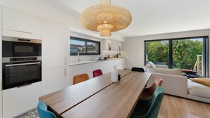 Ett modernt kök med inbyggda vitvaror, en matplats med ett långt träbord och ett stort fönster med utsikt över grönområden.