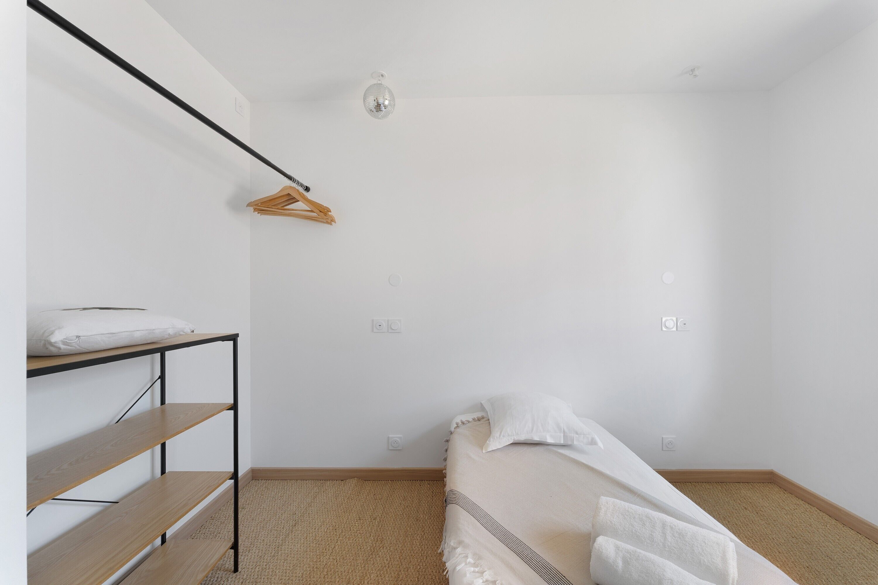 Een kleine, eenvoudig ingerichte kamer met een stapelbed, een houten plank, een hanglamp en een enkel stopcontact.