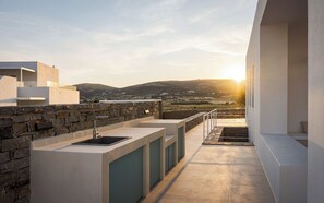 Une cuisine extérieure moderne, avec un mur en pierre, un évier et une vue sur la campagne au coucher du soleil.