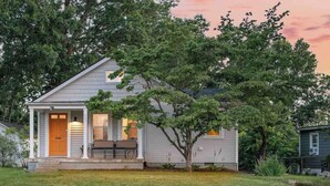 Ein eingeschossiges Haus mit Veranda, kleinem Garten und Baum davor.