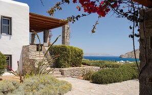 A stone building with a wooden pergola, a stone staircase, and a view of the sea. - Villa Kohyli by Mediterà (Paros)